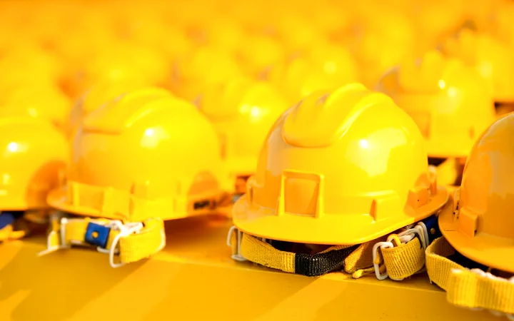 Yellow construction hard hats laid out in rows with chin straps beside them