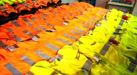 Fluorescent orange and yellow-green high-visibility jackets with silver reflective bands laid out in colour-sorted rows