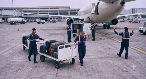 Airport ground handling crew in matching navy coveralls and high-visibility striping working an aircraft apron in India